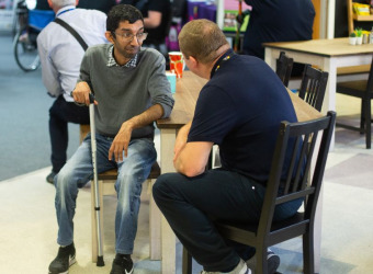 Rupak sitting at a table in The Brain Food café. he's holding a walking stick and speaking to a man.