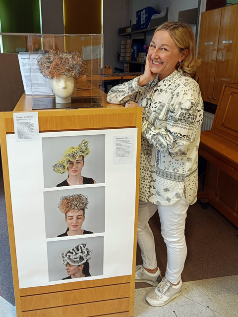 Helen standing next to a display of her work in the form of hats.