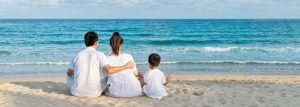 A family sitting on a beach looking out to sea. There are 2 adults and one little boy