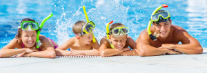 A woman and a man with two boys. They are all in a swimming pool, leaning on the edge and wearing snorkels