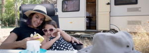 A woman with a child sitting on a chair outside a caravan