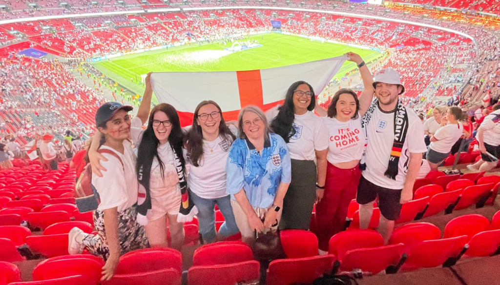 A group of friends with an England flag in a football stadium.