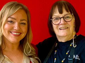 Two women. Kellyann and Rose standing against a plain red background