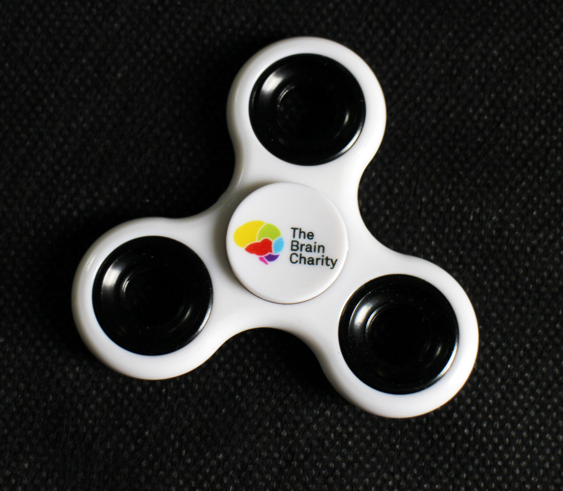 A white fidget spinner with The Brain Charity logo in the centre