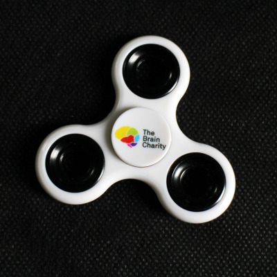 A white fidget spinner with The Brain Charity logo in the centre