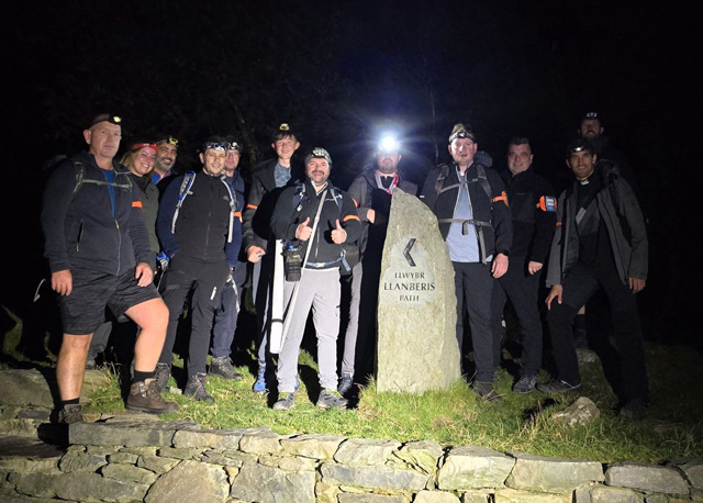 A group of hikers standing by a marker stone at the start of the Llanberis path. It is dark and they have lights on their heads