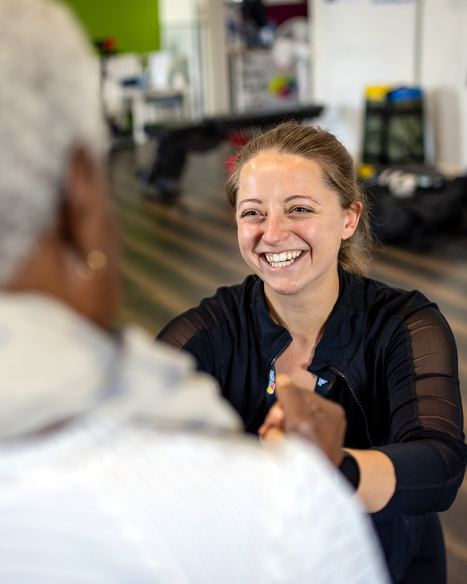 Young woman smiling and holding the hand another woman who's seated during physiotherapy exercise