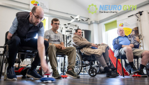 Four people playing new age kurling in The Brain Charity's Neuro Gym. The man closest to the camera is about to roll his puck