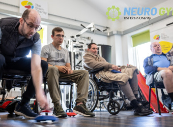 Four people playing new age kurling in The Brain Charity's Neuro Gym. The man closest to the camera is about to roll his puck