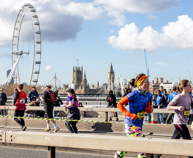 Peope running across a bridge with the London Eye and Houses of Parliament in the background