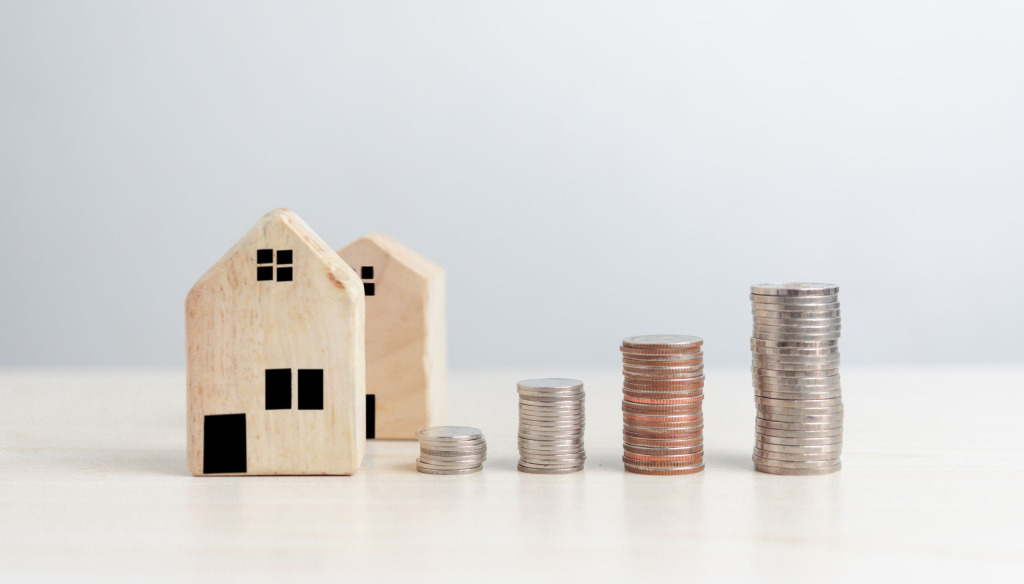 Small wooden houses with increasingly high stacks of coins. Plain background