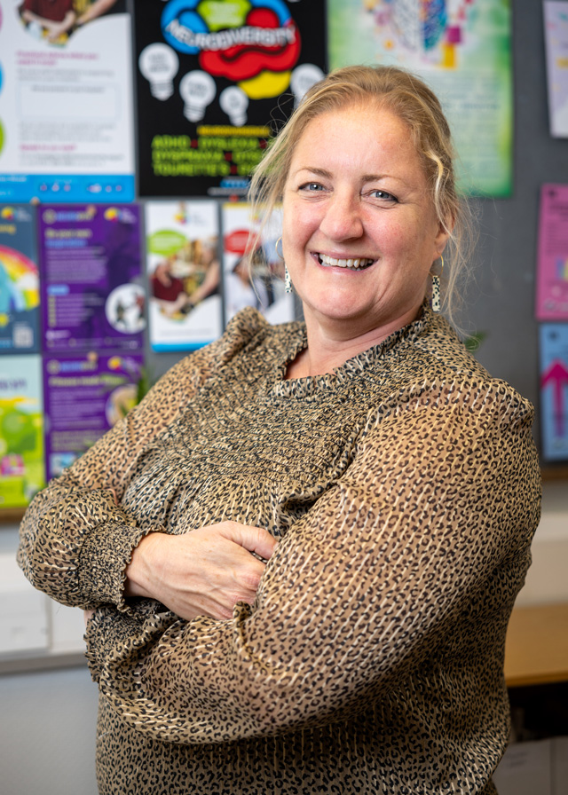 Pippa, a blond woman, standing on front of notice board smiling