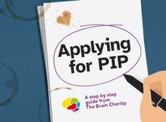 A notepad with the words Applying for PIP. A cartoon hand holding a pen has circled the title. There are coffee stains on it indicating all the hard work that has been put in to the application.