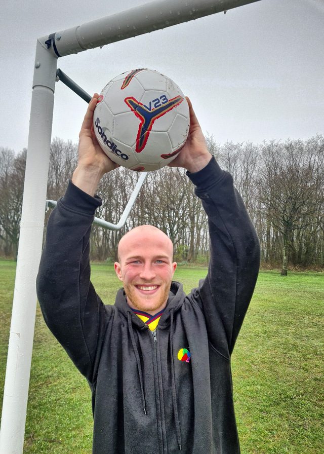 Archie standing in a goal holding a football above his head