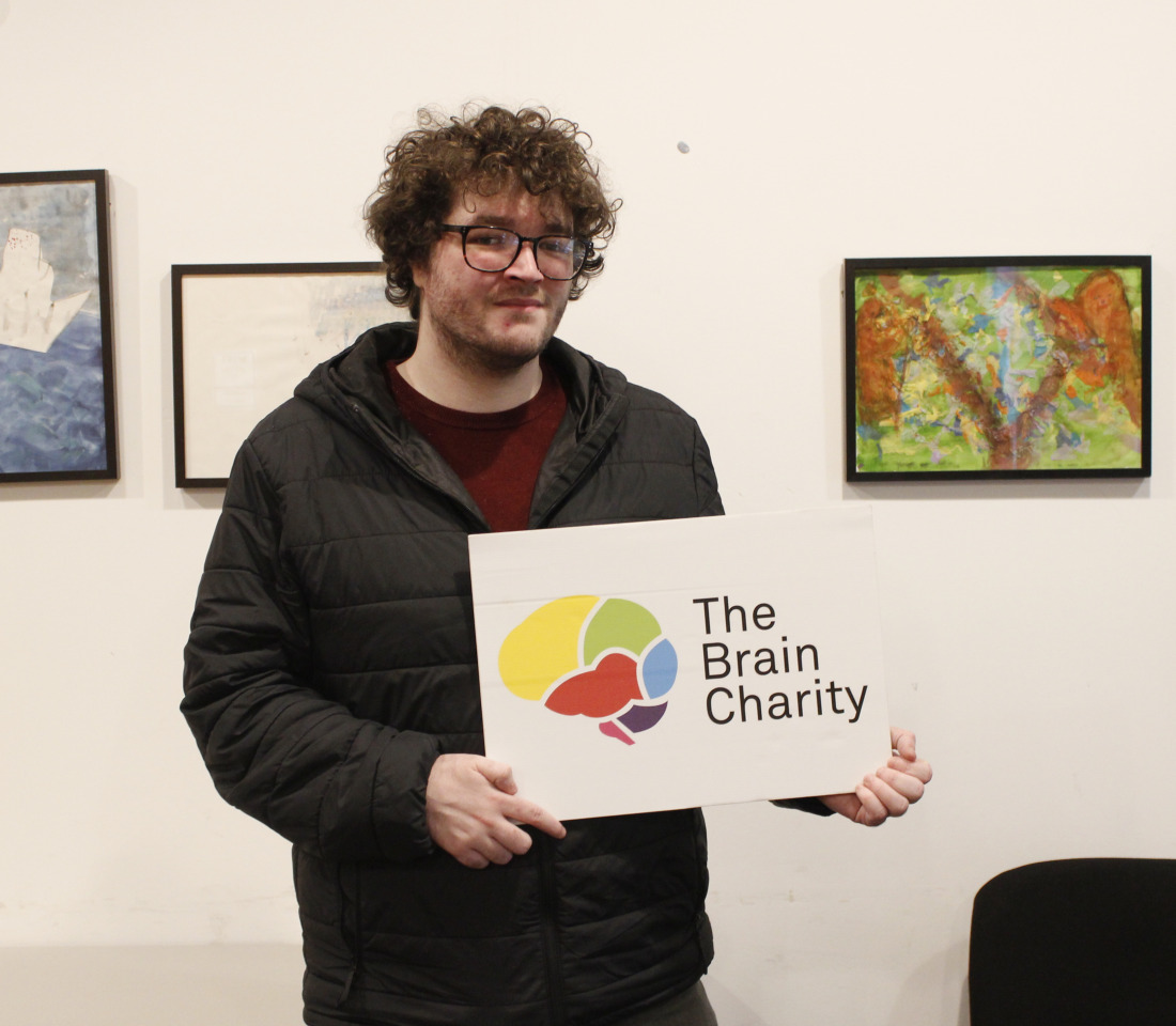 Man (Chris), reciepient of our Confidence coahcing, holding up The Brain Charity logo.