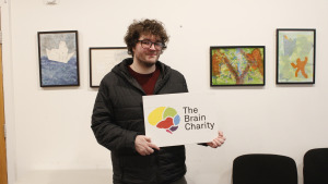 Man (Chris), reciepient of our Confidence coahcing, holding up The Brain Charity logo.