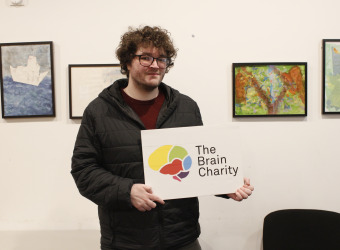 Man (Chris), reciepient of our Confidence coahcing, holding up The Brain Charity logo.